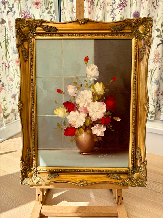 Decorative painting of flowers in a gold frame on an easel with floral wallpaper.