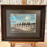 Framed artwork of people on a beach with a brown frame.