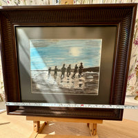 Framed artwork of people on a beach with a ruler for scale.