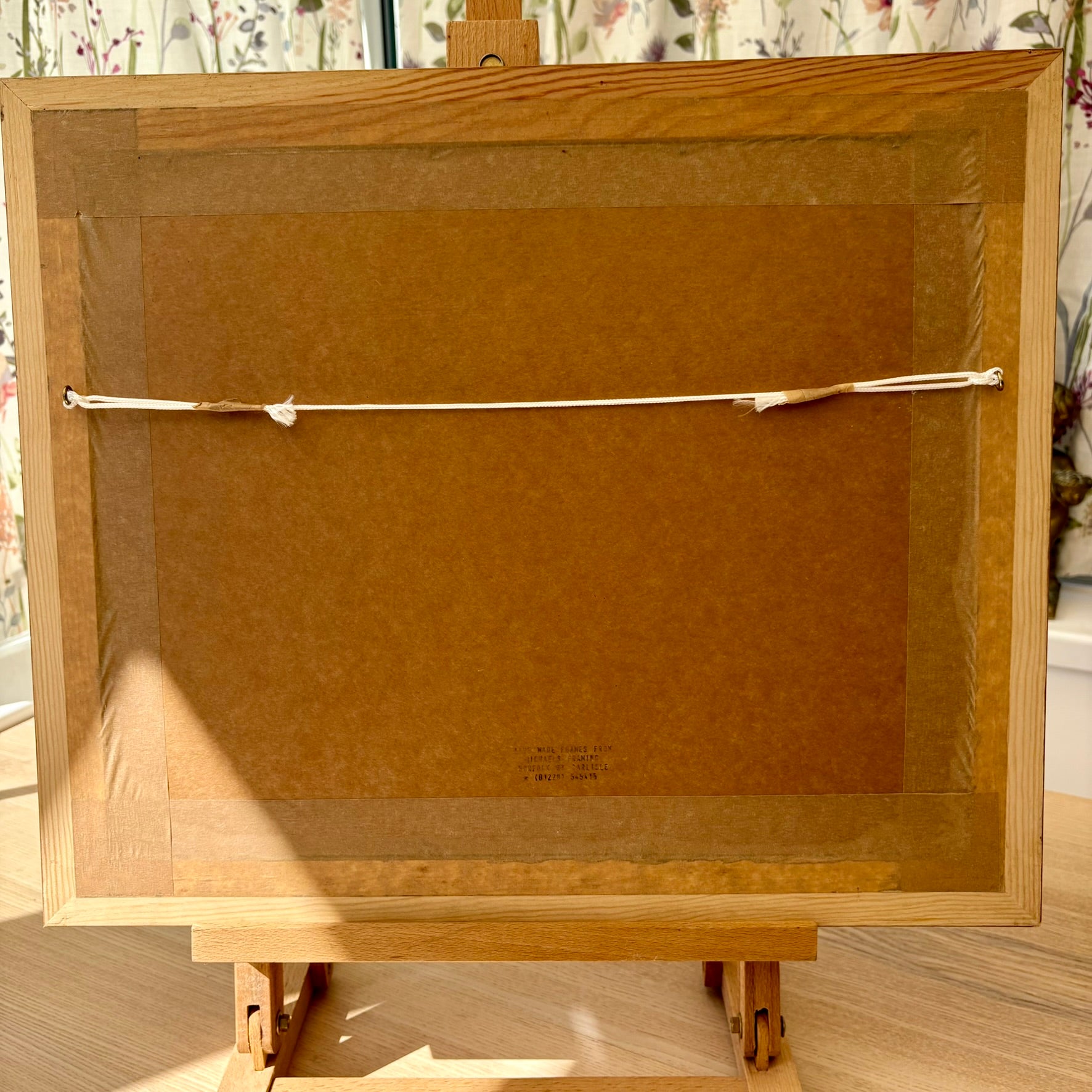 Back view of a wooden picture frame with a brown mat on an easel.