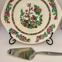 Decorative plate with floral design on a stand, accompanied by a silver spoon.
