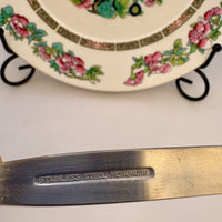 Metallic object with 'Stainless Steel Hong Kong' engraving in front of a floral-patterned plate.
