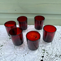 Set of six red-tinted glasses on a white lace tablecloth with a light green wall background.