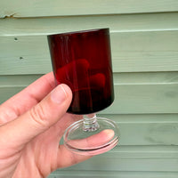Hand holding a red glass against a wooden background
