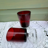 Two red glass tumblers on a white lace tablecloth with a light green wooden surface in the background.