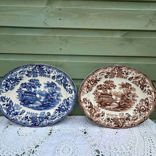 Two decorative plates with blue and brown patterns on a lace tablecloth against a wooden background.