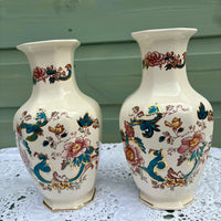 Two decorative vases with floral and peacock patterns on a lace tablecloth.