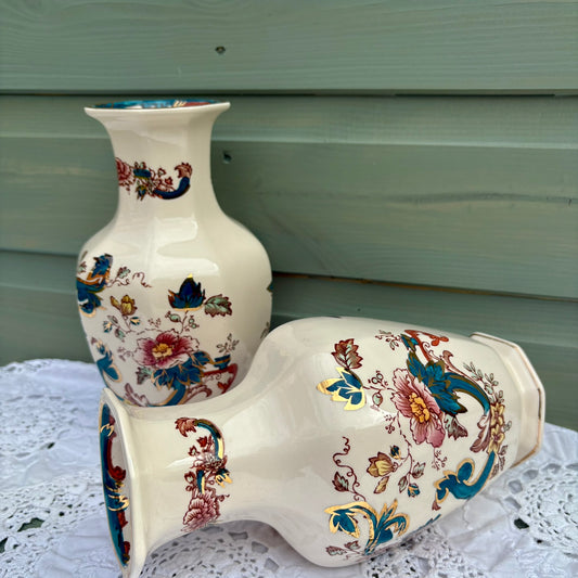 Two ceramic vases with floral patterns on a white surface against a green wooden background