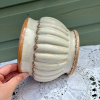 Ceramic vase with ribbed design held by a hand on a lace tablecloth.