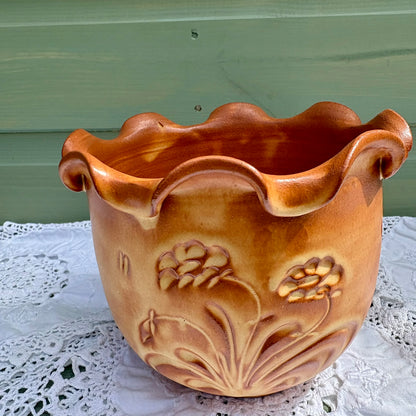 Ceramic planter with floral designs on a lace tablecloth against a green wall.
