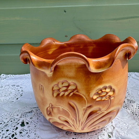 Ceramic planter with floral designs on a lace tablecloth against a green wall.