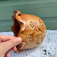 Hand holding a brown ceramic vase with floral patterns on a white lace tablecloth.