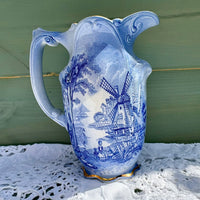 Blue and white ceramic pitcher with windmill design on a lace tablecloth.