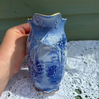 Hand holding a blue ceramic vase with intricate designs on a lace tablecloth.