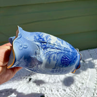 Hand holding a blue and white decorative vase with intricate patterns on a light green background.