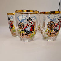 Three glass tumblers with decorative designs of a woman spinning on a wheel, set against a plain background.