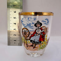 Decorative glass with a printed design of a woman spinning, next to a ruler for scale.