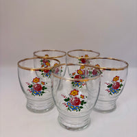Set of five glass tumblers with floral designs and gold rims on a white background
