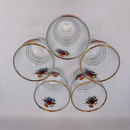 Set of five clear glasses with floral designs and gold rims on a white background