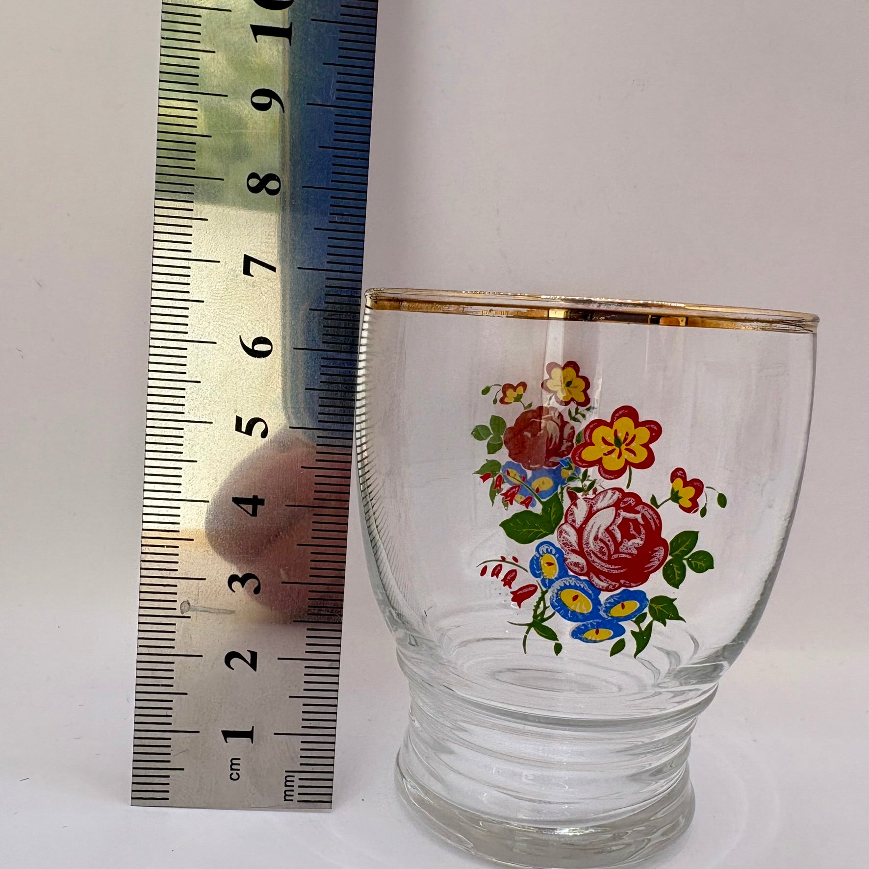 Glass tumbler with floral design next to a ruler on a white background