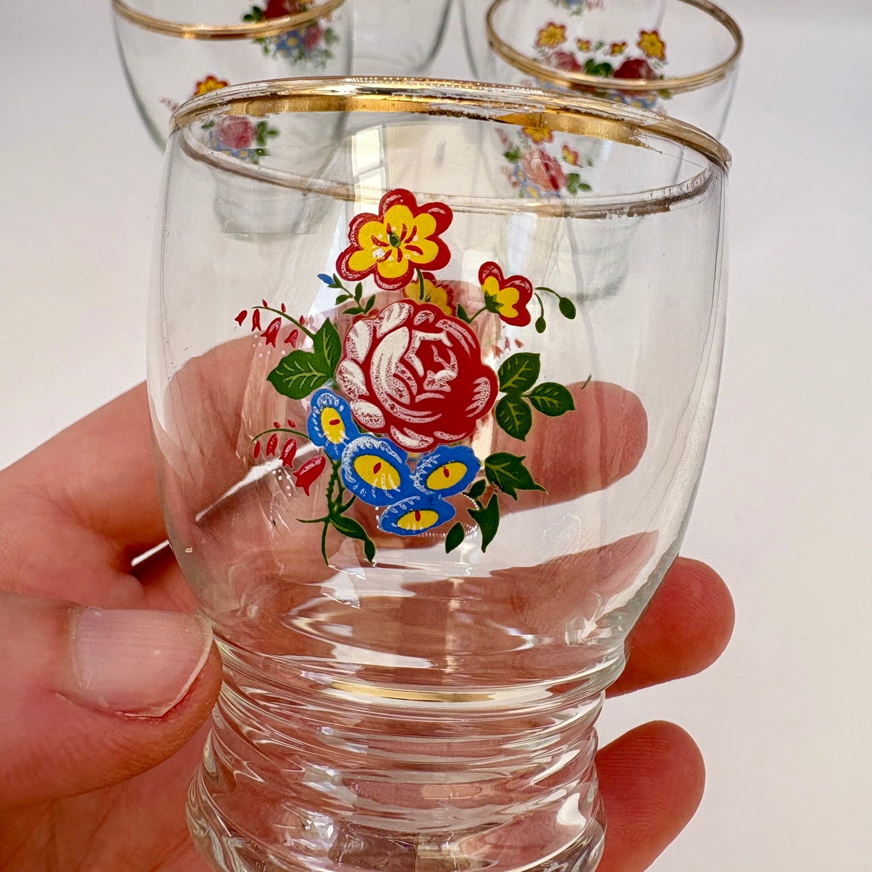 Clear glass with floral design held by a hand against a white background