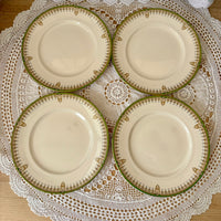 Four ceramic plates with decorative green rims on a lace doily.