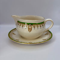 Decorative ceramic creamer and saucer with gold and green patterns on a white background