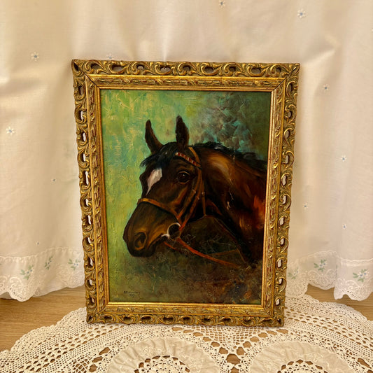 Oil painting of a horse head in an ornate gold frame on a lace tablecloth.