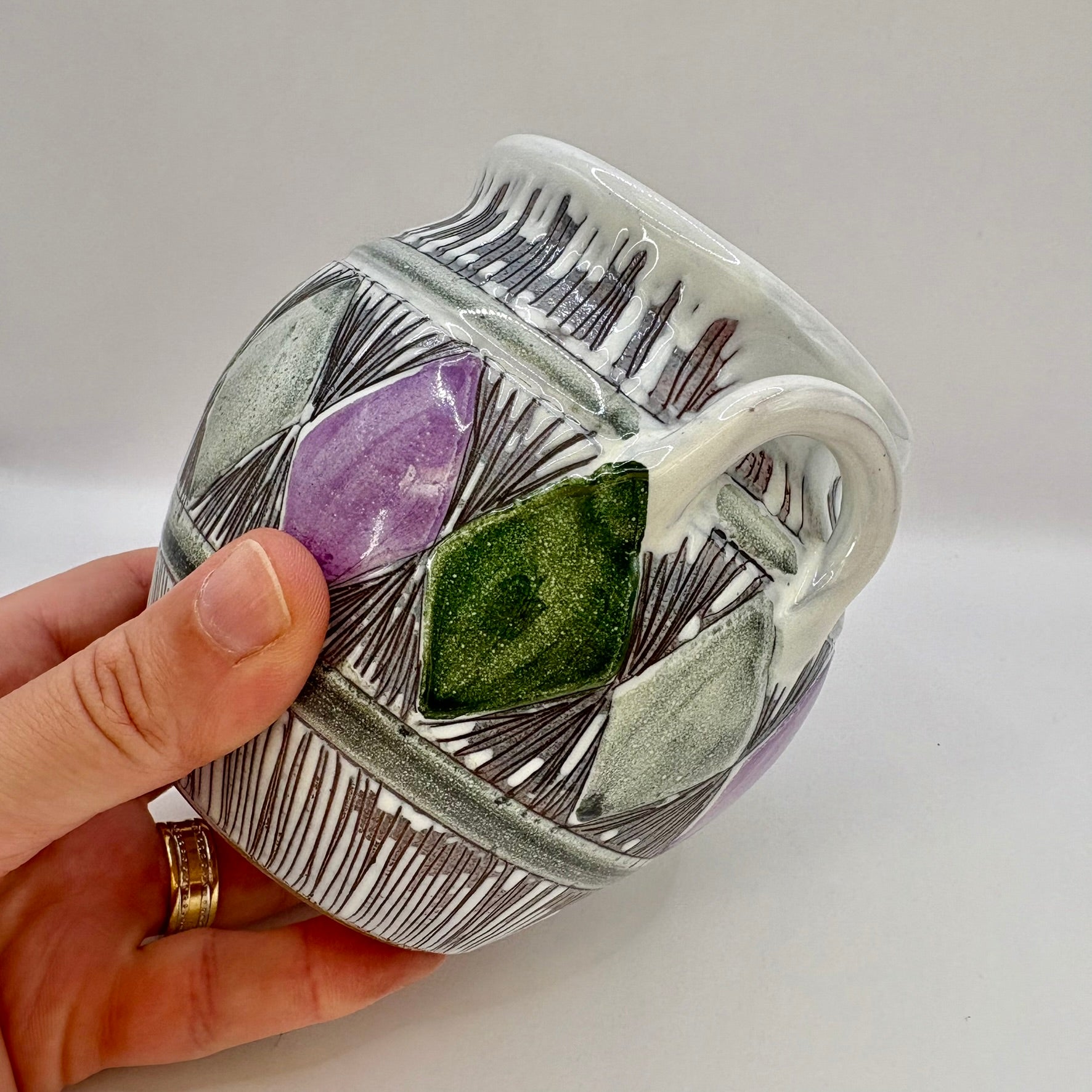 Hand holding a ceramic container with embedded stones against a neutral background