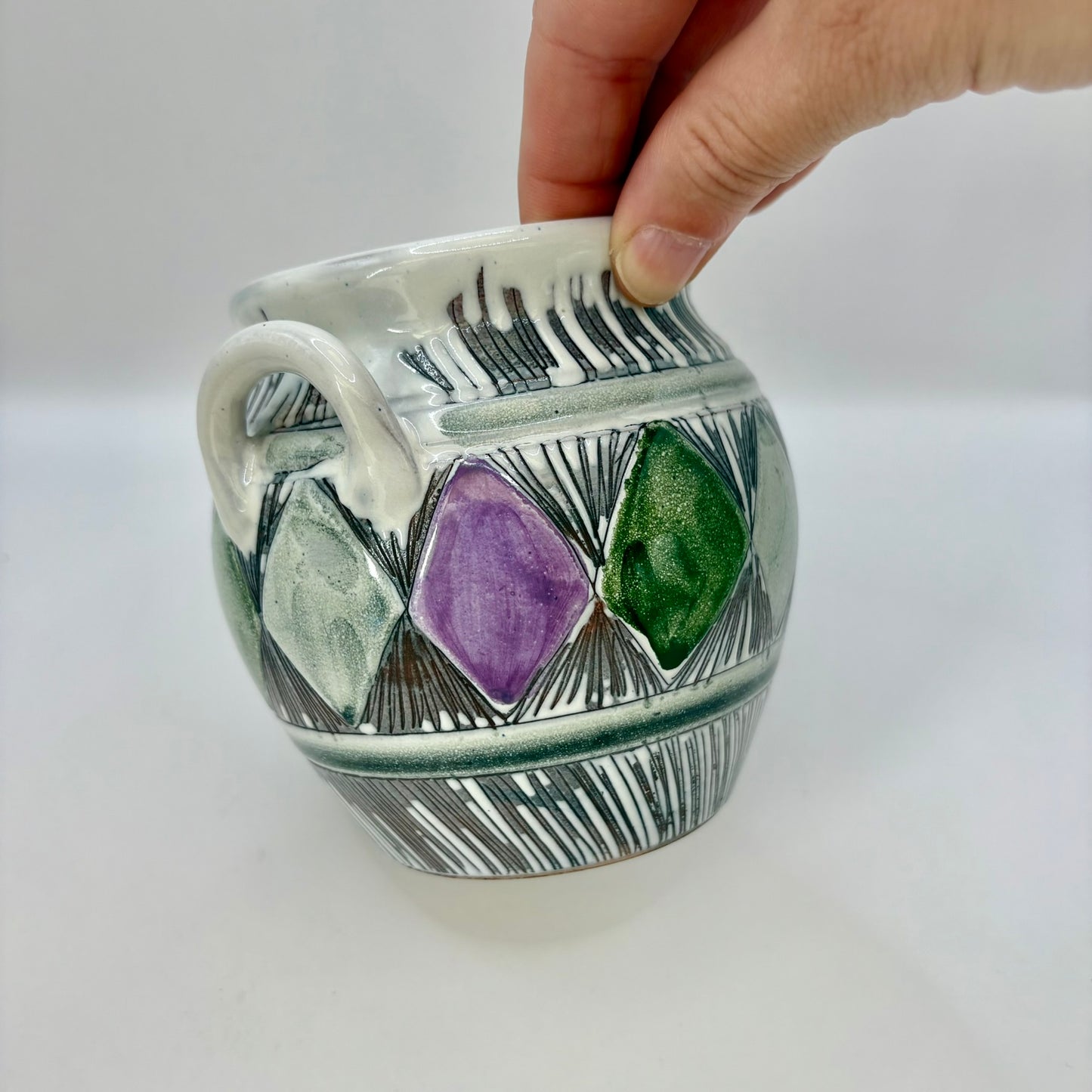 Ceramic mug with geometric design and hand holding it on a white background