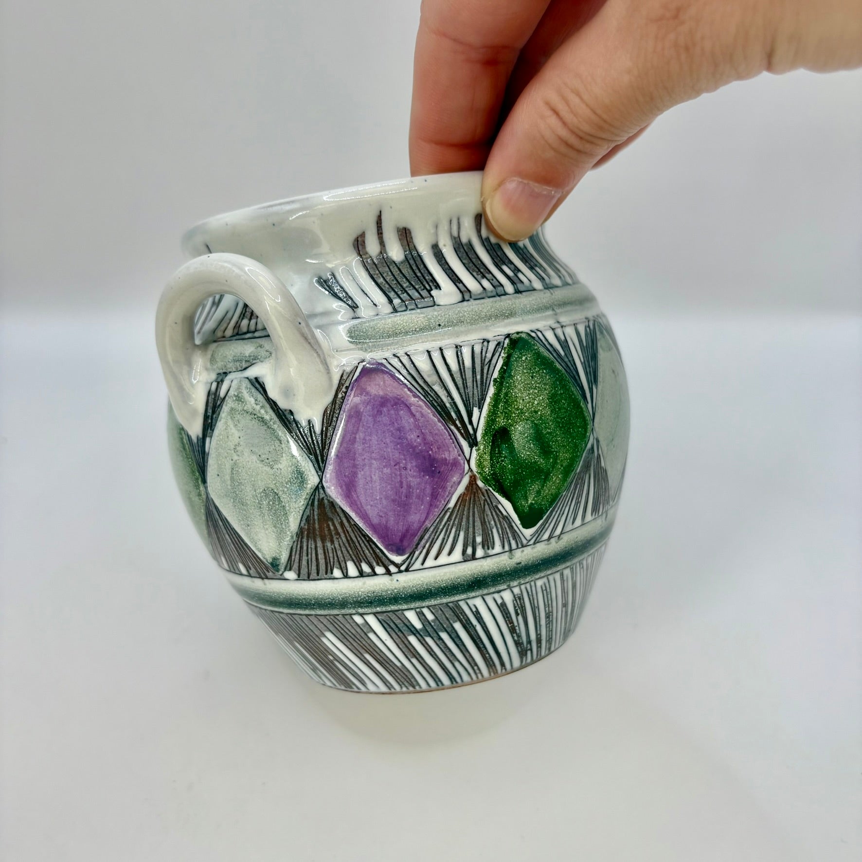 Ceramic mug with geometric design and hand holding it on a white background