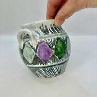 Ceramic mug with geometric design and hand holding it on a white background