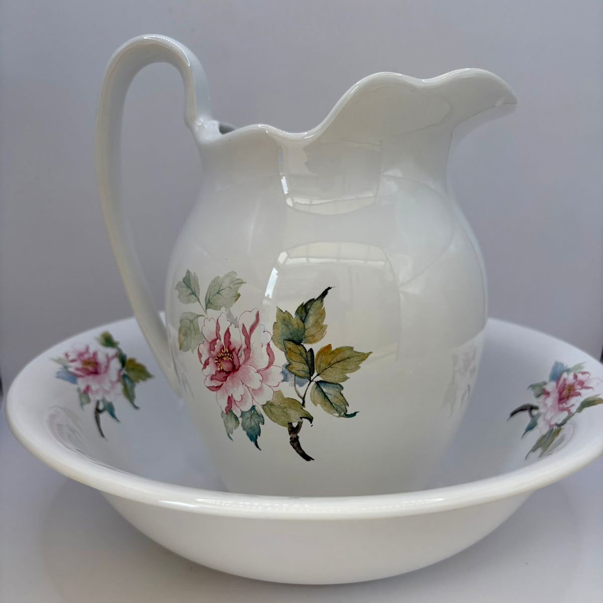 White ceramic pitcher and bowl with floral designs on a white background