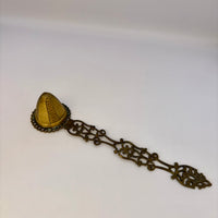 Decorative bronze spoon with a small container on a white background
