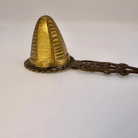 Brass cone-shaped object with chain on a white background