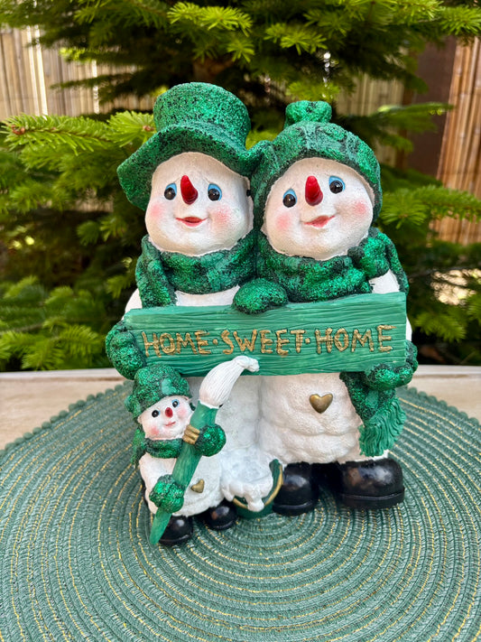 Two snowmen holding a 'Home Sweet Home' sign with a Christmas tree in the background.