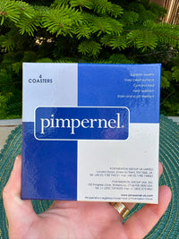 Box of Pimpernel coasters held in front of a green background