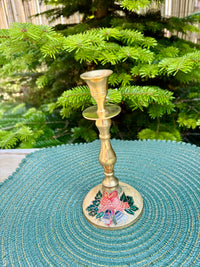 Gold candlestick with floral design on a teal surface with green foliage in the background