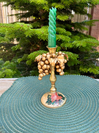 Decorative candle holder with a green candle on a textured surface with a Christmas tree in the background.