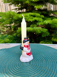 Snowman candle holder with a candle on a textured surface with a green background