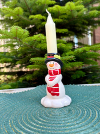 Snowman candle holder with a candle on a textured surface with a blurred green background