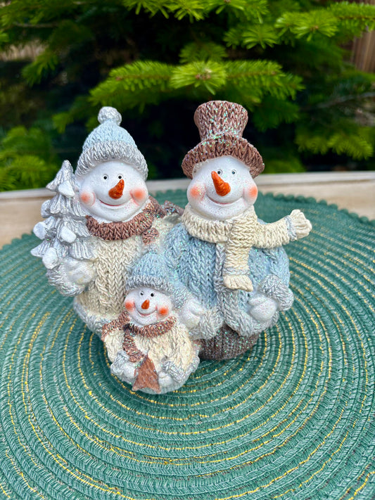 Three snowman figurines with different sizes on a textured surface with a blurred green background
