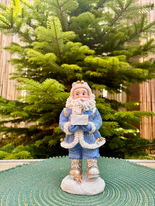 Decorative figure of a person in winter clothing holding a book, with a Christmas tree in the background.
