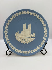 Blue decorative plate with white emblem and text on a stand against a white background
