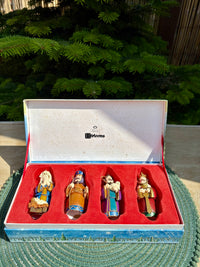 Set of four figurines in a decorative box with a Christmas tree in the background.