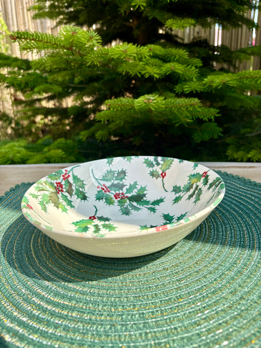 Decorative bowl with holly design on a green woven mat outdoors.