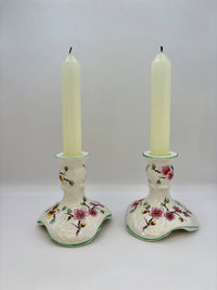 Two ceramic candle holders with floral designs holding candles on a white background