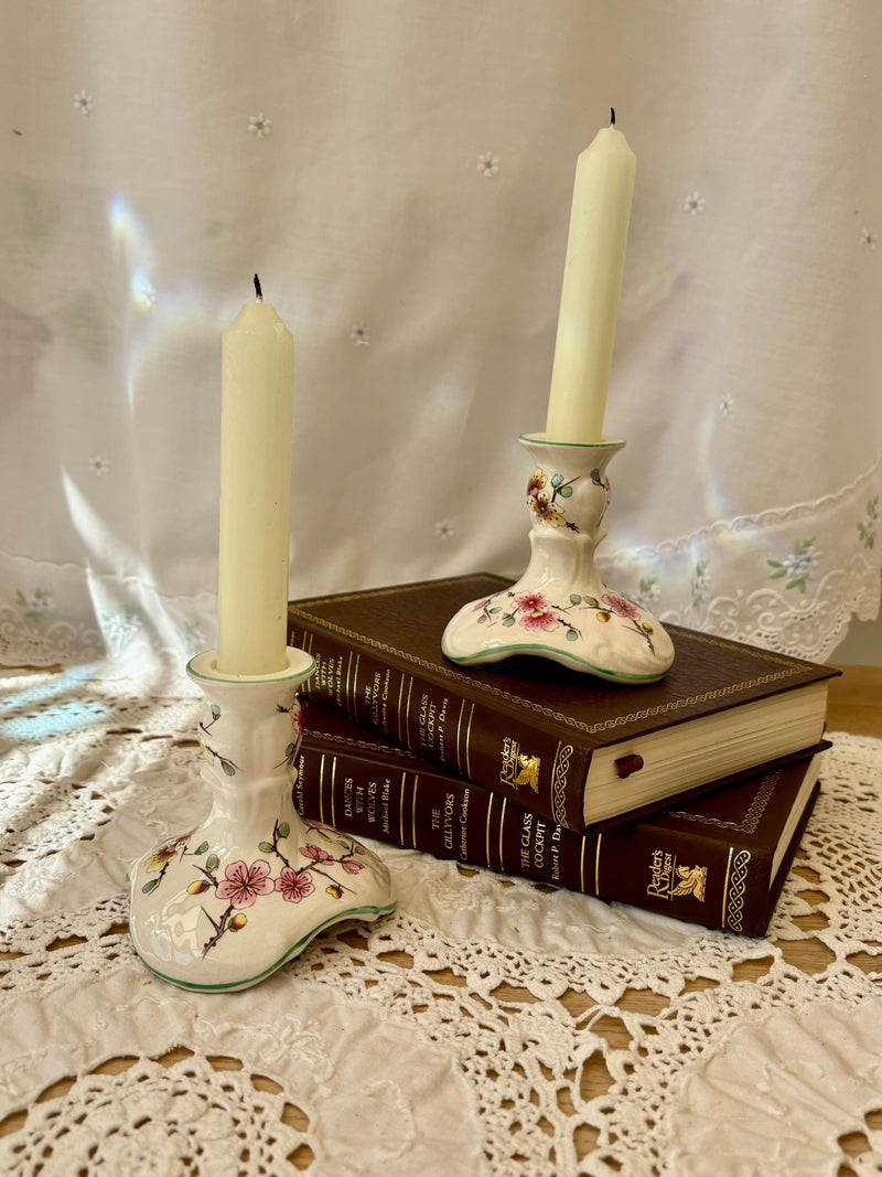 Decorative candlesticks with floral designs on a stack of books against a lace curtain background.