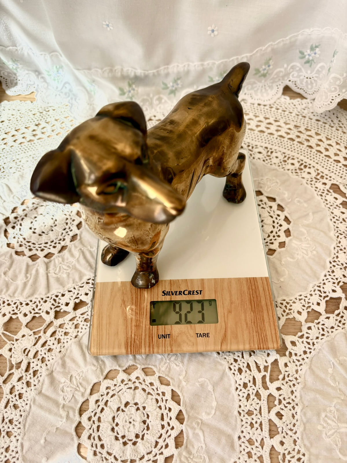 Bronze dog-shaped object on a digital scale with a white lace tablecloth background
