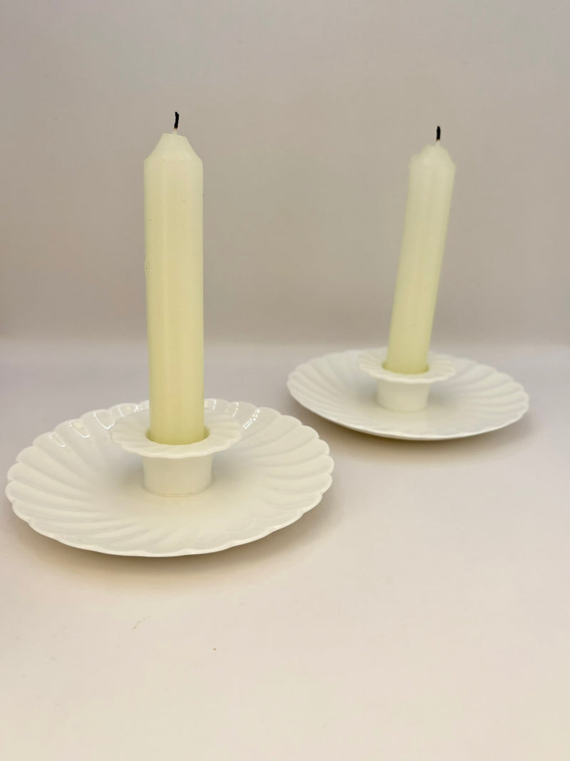 Two white candle holders with candles on a light gray background